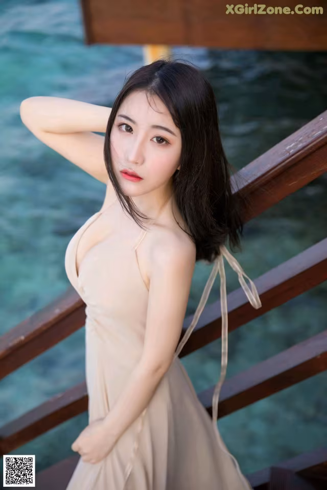 A woman in a beige dress leaning against a wooden railing.