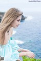 A woman in a blue dress sitting on a rock by the ocean.