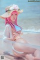 A woman in a bikini and hat sitting on the beach.