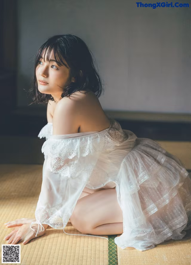 A woman in a white dress sitting on a mat.