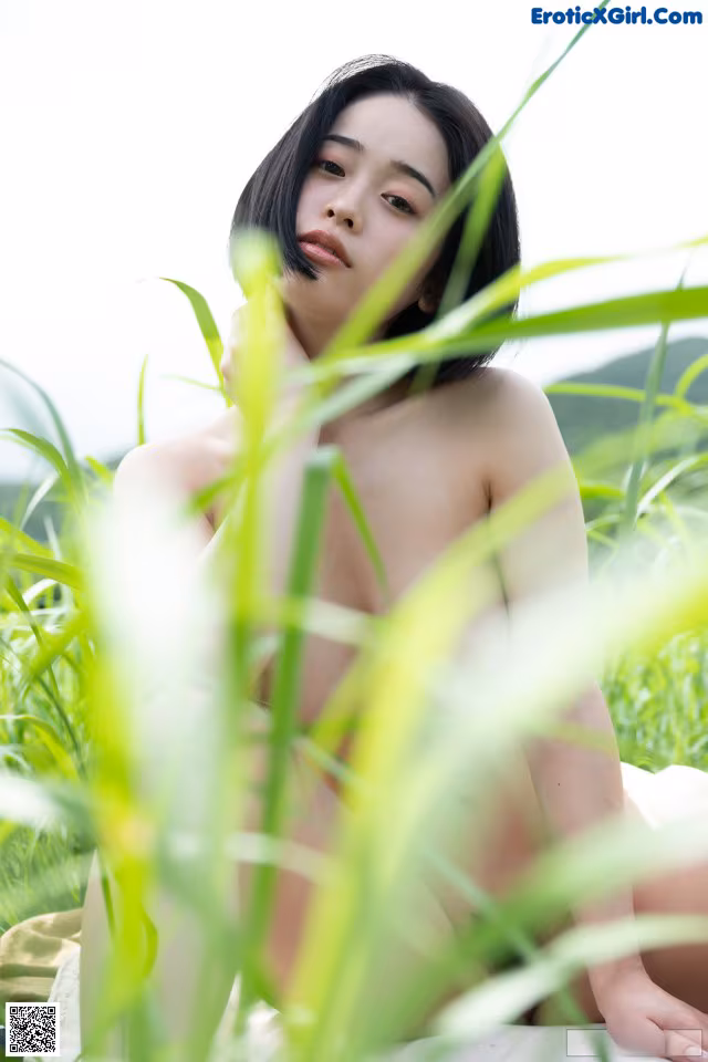 A naked woman sitting in a field of tall grass.