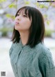 A woman in a green shirt blowing a flower.