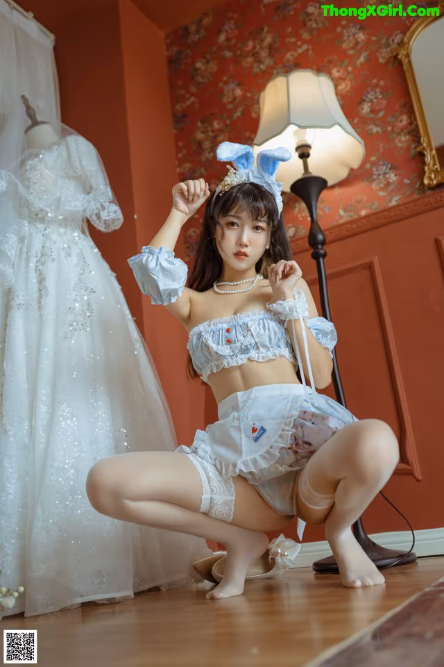 A woman in a white dress sitting on the floor next to a dress form.