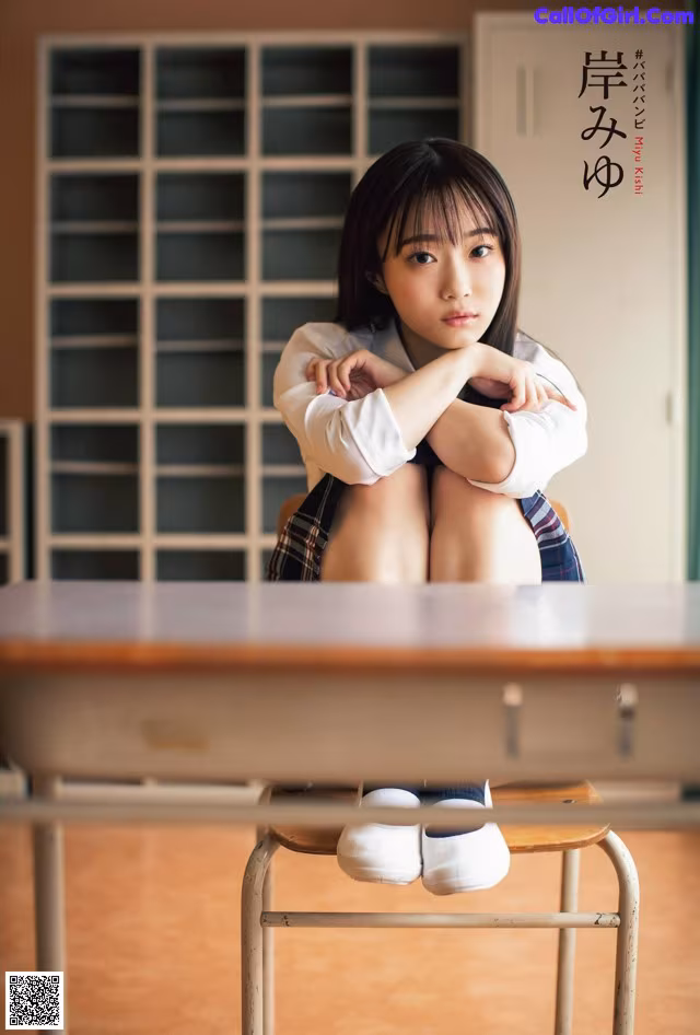 A woman sitting on top of a desk in a classroom.