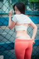 A woman in a white top and red leggings leaning against a fence.