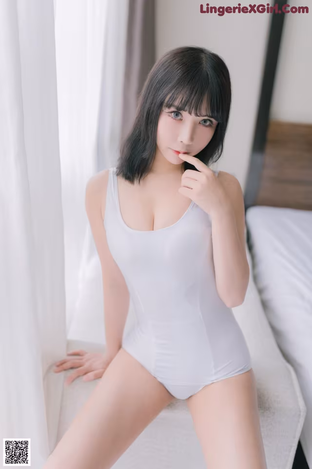 A woman in a white bodysuit sitting on a bed.