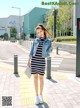 A woman in a striped dress and denim jacket is standing on the sidewalk.