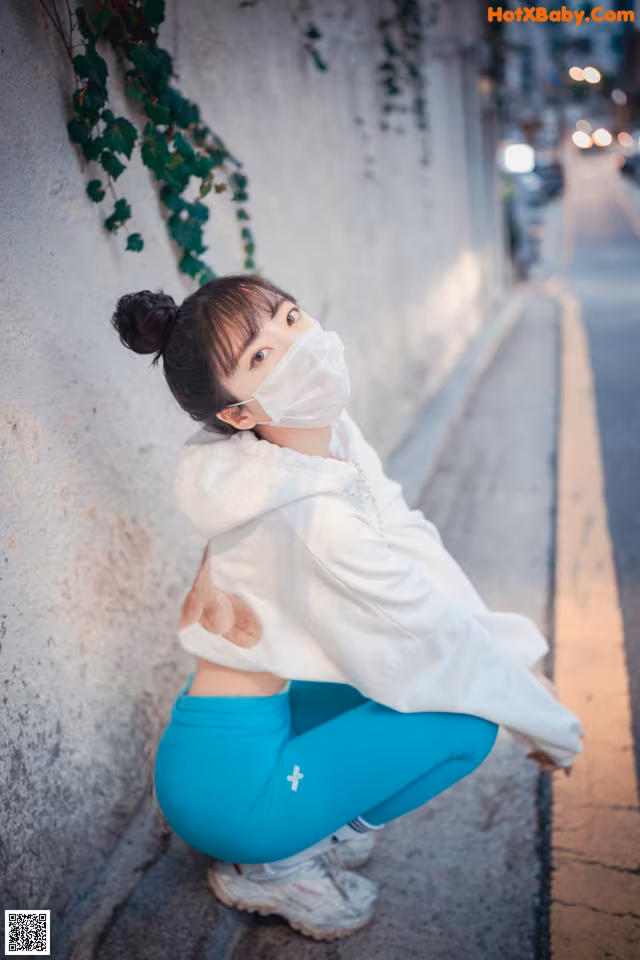 A woman wearing a face mask sitting on the side of a street.