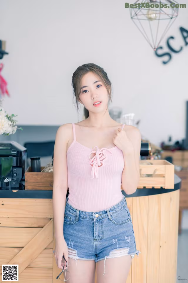 A woman in a pink top and denim shorts posing for a picture.