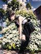 A girl in a school uniform leaning against a bush of flowers.