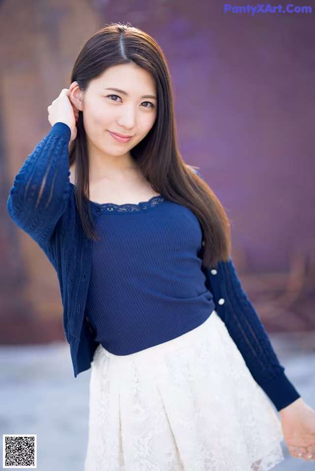 A woman in a blue sweater and white skirt posing for a picture.